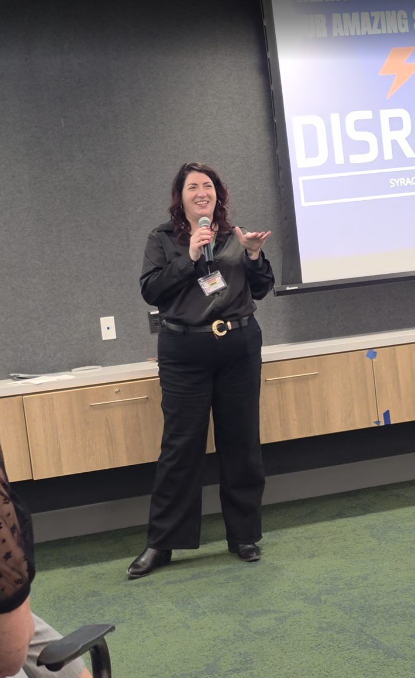 Lindsay Mastro speaking with a microphone in front of a DisruptHR Syracuse screen
